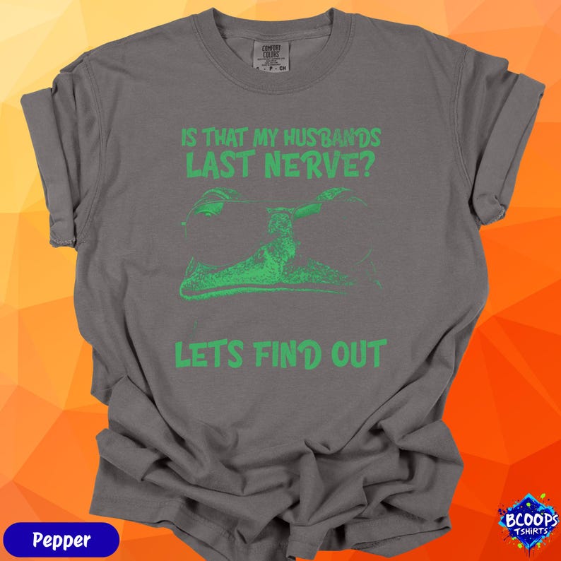 A green sunglasses-wearing frog with playful text reading “Is That My Husbands’s Last Nerve? Let’s Find Out.” The design pops on the pepper color, creating a fun, cheeky look wives and moms will love.