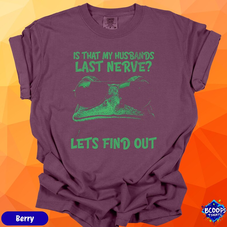 A bright green frog wearing sunglasses with the text “Is That My Husbands’s Last Nerve? Let’s Find Out.” The humorous design contrasts boldly with the berry shirt, giving it a fun, vibrant personality perfect for gifting.