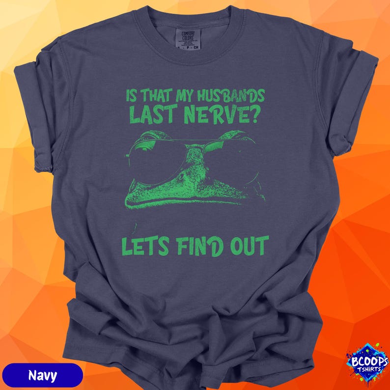 A green frog in sunglasses paired with the phrase “Is That My Husbands’s Last Nerve? Let’s Find Out.” The crisp green graphic contrasts well with the navy shirt, creating a bold and funny design ideal for wives who enjoy lighthearted marital jokes.