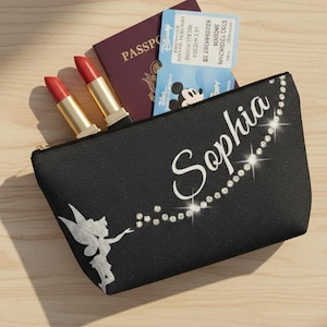 Könnte beinhalten: Schwarze Kosmetiktasche mit dem Namen "Sophia" in weißer Schrift und einer Tinkerbell-Grafik. Die Tasche enthält zwei Lippenstifte, einen Reisepass und Disney-Parkkarten. Mit Reißverschluss.