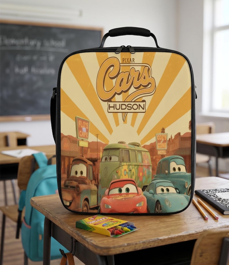 Puede incluir: Una bolsa de almuerzo rectangular con un gr&aacute;fico de Pixar Cars que muestra a los personajes Rayo McQueen, Mate, Fillmore y Sally. El dise&ntilde;o incluye un fondo de rayos de sol amarillos, el texto Cars y Hudson, y letreros de Flo's V8 Cafe y Cozy Cone.