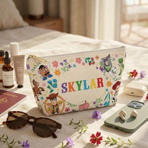 Puede incluir: Un neceser beige con cremallera dorada, con coloridos dise&ntilde;os florales y personajes de Toy Story. El nombre "SKYLAR" est&aacute; impreso en letras de arco&iacute;ris. Otros art&iacute;culos incluyen gafas de sol, pasaporte y productos para el cuidado de la piel.