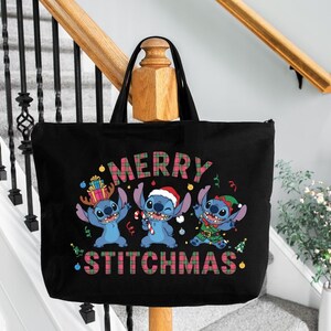 May include: Black tote bag with a festive design featuring three blue cartoon characters. The bag displays the words "MERRY STITCHMAS" in a plaid pattern. The characters are dressed in Christmas attire, including a Santa hat.