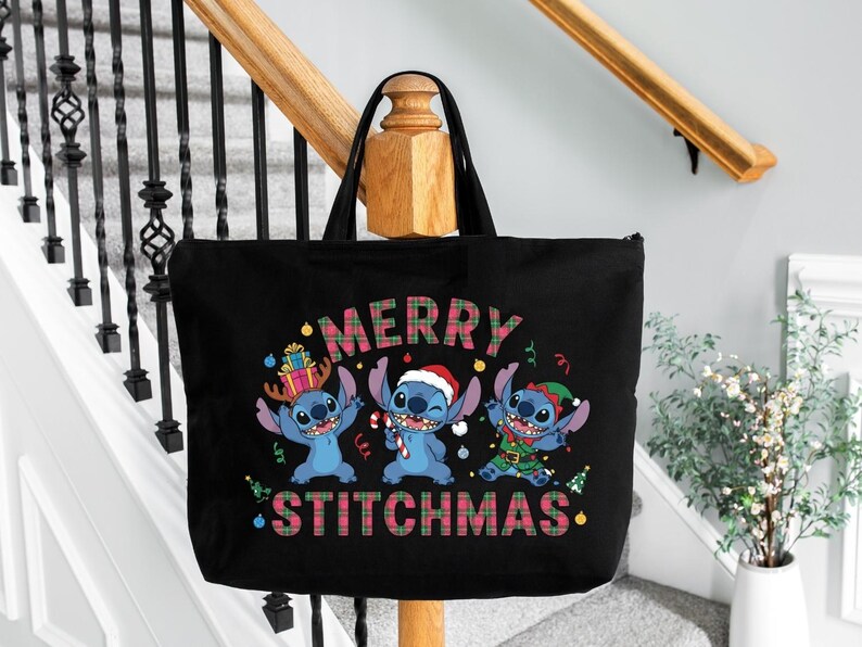 May include: Black tote bag with a festive design featuring three blue cartoon characters. The bag displays the words "MERRY STITCHMAS" in a plaid pattern. The characters are dressed in Christmas attire, including a Santa hat.