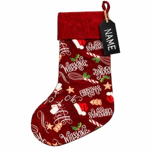 May include: A deep red Christmas stocking featuring a repeating pattern of white whisk illustrations, candy canes, Santa hats, and the text "Whisking you a Merry Christmas" and "No cookie left behind." A black rectangular tag labeled "NAME" is attached.