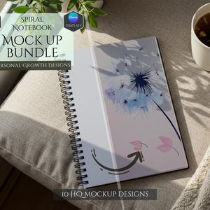 May include: A spiral notebook mockup with a dandelion design on the cover. The notebook is lying open on a beige surface with a cup of tea and a white blanket.