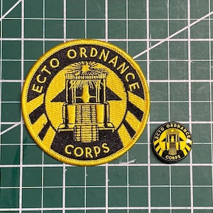 May include: A black and yellow embroidered patch with the text "ECTO ORDNANCE CORPS" and a stylised image of a building. A smaller, black and yellow button with the same design is also shown.