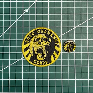 May include: A yellow and black embroidered patch with the text "ECTO ORDNANCE CORPS" and a skull with a screaming mouth. A smaller, similar pin is also shown.
