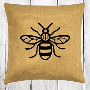 May include: A yellow throw pillow with a black bee design. The bee has black and white stripes and is centred on the pillow.
