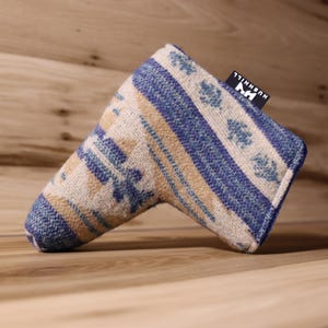 Op de afbeelding: Een golfclub putterhoes met een blauw, beige en wit geometrisch patroon. De hoes heeft een rechthoekige vorm met een afgerond uiteinde en een klein zwart label met witte tekst. De hoes is gemaakt van een geweven stof.