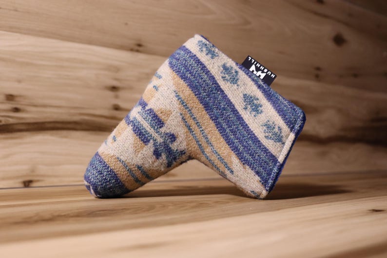 Op de afbeelding: Een golfclub putterhoes met een blauw, beige en wit geometrisch patroon. De hoes heeft een rechthoekige vorm met een afgerond uiteinde en een klein zwart label met witte tekst. De hoes is gemaakt van een geweven stof.