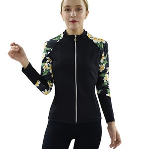 May include: A black zip-up jacket with long sleeves and a high collar. The sleeves feature a floral pattern with yellow and white flowers on a black background. The jacket has a white zipper and a fitted silhouette.