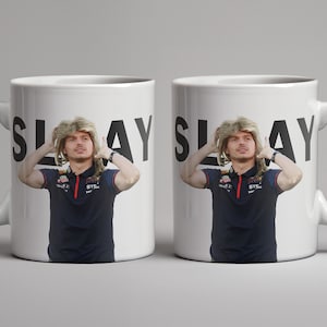 May include: Two white ceramic mugs with black text that reads "SLAY" and a photo of a person with blonde hair. The person is wearing a blue polo shirt with a red logo.