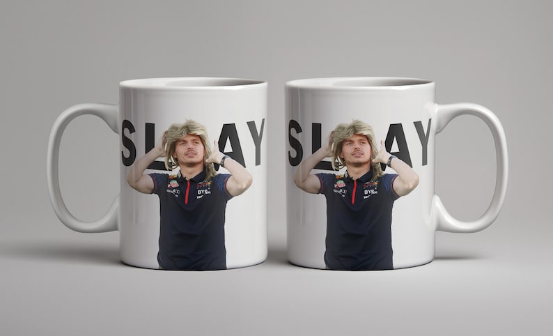May include: Two white ceramic mugs with black text that reads "SLAY" and a photo of a person with blonde hair. The person is wearing a blue polo shirt with a red logo.