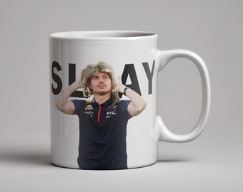 May include: White ceramic mug with a black and white image of a person with blonde hair wearing a black shirt with red and white accents. The text "SLAY" is printed on the mug.