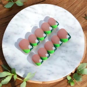 May include: Set of ten short, oval-shaped false nails with a light pink base and a green and white shamrock design.