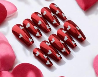 May include: Set of ten red coffin-shaped false nails with white heart designs.
