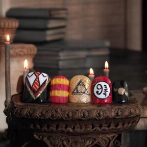 Puede incluir: Cinco anillos para uñas con diferentes diseños temáticos de Harry Potter. Los anillos son rojos, dorados, negros, amarillos y negros con detalles dorados. Los diseños incluyen un uniforme de Hogwarts, una bufanda de Gryffindor, el símbolo de las Reliquias de la Muerte, el letrero de la Plataforma 9 3/4 y una snitch dorada.