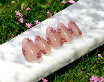 May include: Set of six pink almond-shaped press-on nails with a floral design. The nails have a light pink base with a darker pink floral pattern.