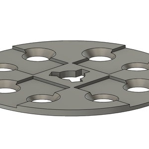 May include: A grey metal disc with six circular cutouts and a smaller, irregular cutout in the centre. The disc has a slightly raised edge.