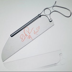 May include: A silver surgical saw with a handle and a serrated blade. The blade has red writing on it that says "8-20" and "Marie".