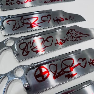May include: Four silver hand saws with red graffiti art. The saws have a heart, a bird, and other abstract designs. The text on the saws reads "2 love Medic!!!".