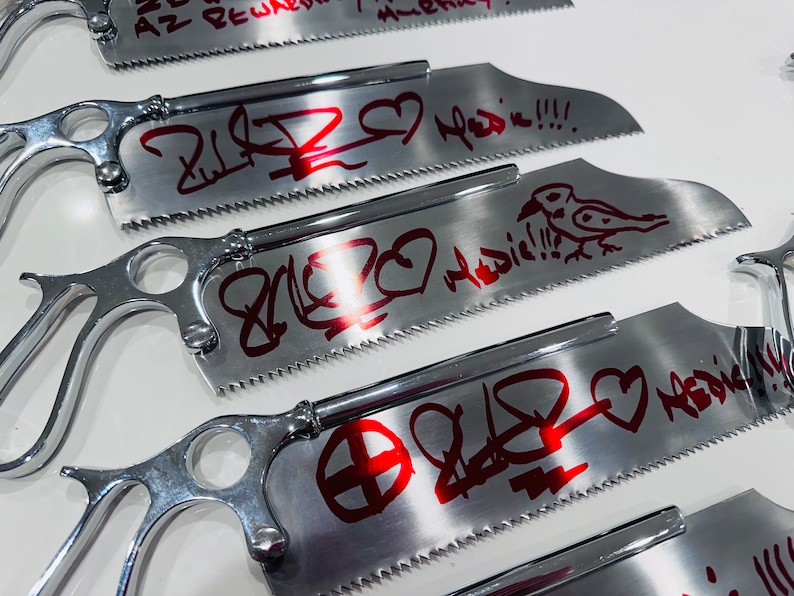 May include: Four silver hand saws with red graffiti art. The saws have a heart, a bird, and other abstract designs. The text on the saws reads "2 love Medic!!!".