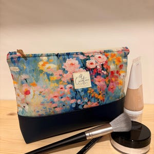 Peut inclure: Une pochette rectangulaire en tissu avec un imprimé floral coloré sur la partie supérieure et une base bleu marine unie. Une étiquette beige avec le texte Creation Cathy est centrée sur le devant. Un pinceau, un crayon, un tube et un pot sont présents.