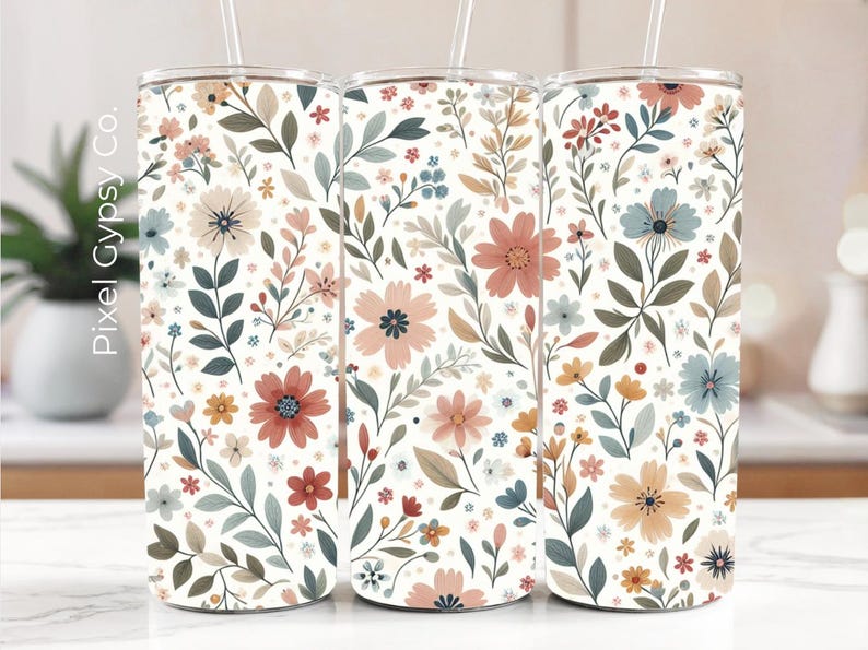 Op de afbeelding: Drie roestvrijstalen bekers met een witte achtergrond en een bloemenpatroon in roze, blauwe en groene tinten. De bekers zijn allemaal even groot en hebben een rietje.