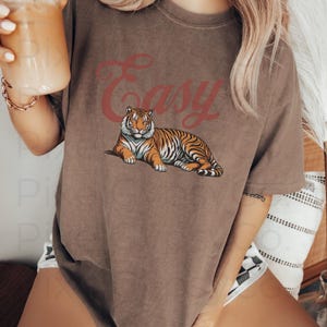 May include: A brown oversized t-shirt with the word "Easy" printed in red script and a tiger illustration.