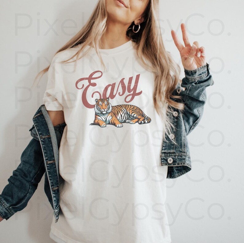 May include: White t-shirt with the word "Easy" in red script and a tiger illustration. The model is wearing a denim jacket.