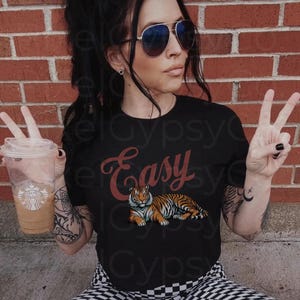 May include: A black t-shirt with the word "Easy" in red cursive lettering and a tiger illustration. The tiger is orange and black with a white background.