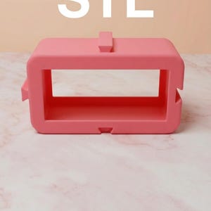 Könnte beinhalten: Ein leuchtend rosa rechteckiges Objekt mit den weißen Buchstaben "STL" oben. Das Objekt hat eine rechteckige Öffnung in der Mitte und eine kleine Lasche oben. Es liegt auf einer rosa Oberfläche.