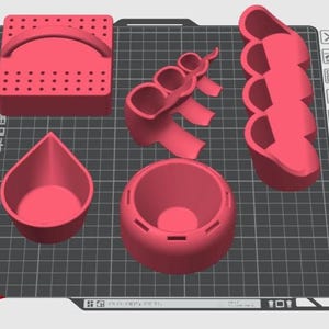 Pode incluir: Uma coleção de objetos vermelhos impressos em 3D, incluindo um bloco retangular com uma alça, um recipiente em forma de gota, um recipiente redondo e duas outras formas multi-seccionadas. Os objetos estão dispostos em uma grade cinza.