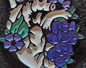 May include: A white anatomical heart with a detailed design, surrounded by purple and green flowers. The heart is outlined in black and has a glossy finish.