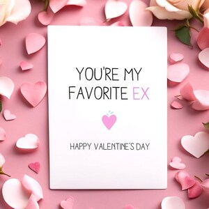 May include: A white greeting card with the text "YOU'RE MY FAVORITE EX" and "HAPPY VALENTINE'S DAY" on a pink background. The card features a pink heart graphic and is surrounded by pink heart-shaped decorations and rose petals.
