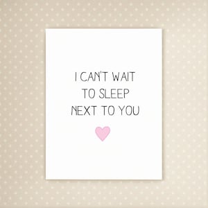 May include: A white card with the text "I CAN'T WAIT TO SLEEP NEXT TO YOU" in black. A pink heart is below the text. The background is a light beige with small white polka dots.