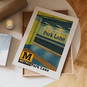 May include: A print of a subway station, featuring the words "Park Lane" in blue lettering. The artwork has a retro style with yellow and blue tones, and the Metro logo is visible. The print is displayed on a white surface.