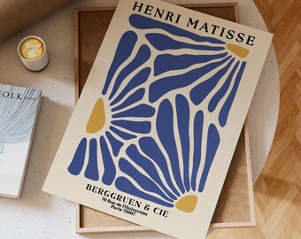 Puede incluir: Una impresión artística enmarcada con un diseño floral en azul y amarillo sobre un fondo crema. La impresión incluye el texto "HENRI MATISSE" en la parte superior y "BERGGRUEN & CIE" con una dirección en la parte inferior. La obra de arte se muestra en una bandeja de madera.