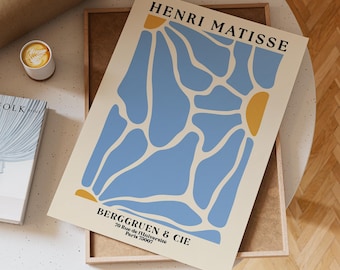 Puede incluir: Una impresión artística enmarcada con un diseño abstracto azul y amarillo, con el texto "HENRI MATISSE" en la parte superior. La impresión también incluye el texto "BERGGRUEN & CIE" y detalles de la dirección. La obra de arte se muestra sobre una superficie blanca.