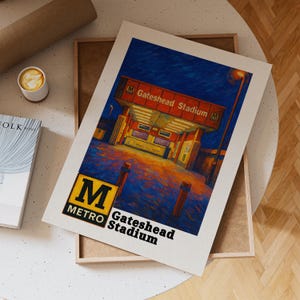 May include: An art print depicting Gateshead Stadium at night. The print features a colour palette of blues, oranges, and yellows, with the text "M Metro Gateshead Stadium" at the bottom. The print is displayed in a wooden frame.