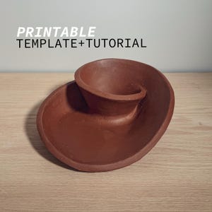 Può includere: Una ciotola in ceramica marrone con un design unico e a spirale. La ciotola è realizzata in argilla e ha una superficie testurizzata. È un modello e un tutorial stampabili.
