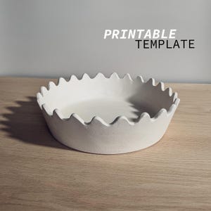 May include: Printable template for a white ceramic bowl with a wavy rim. The bowl is on a light brown wooden surface.