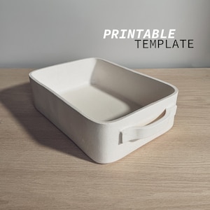 Può includere: Un vassoio rettangolare bianco con un manico su un lato. Il vassoio è realizzato in un materiale strutturato ed è vuoto. Il vassoio è appoggiato su una superficie di legno. PRINTABLE TEMPLATE è scritto in nero sopra il vassoio.