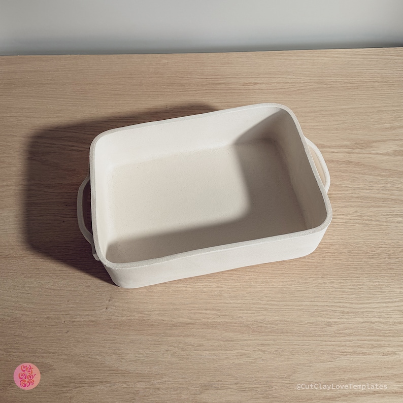 May include: A rectangular off-white ceramic baking dish with rounded corners and two side handles. The surface has a matte, unglazed texture. A small pink circular logo with the text Cut Clay Love is in the corner, and the text CutClayLoveTemplates.