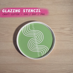 以下が含まれることがあります： 木製の表面に白い波状の線が引かれた緑色の円。円の上に「Glazing Stencil」というテキストがあります。円の下に「Craft Cutter ~ SVG / DXF / PNG」というテキストがあります。