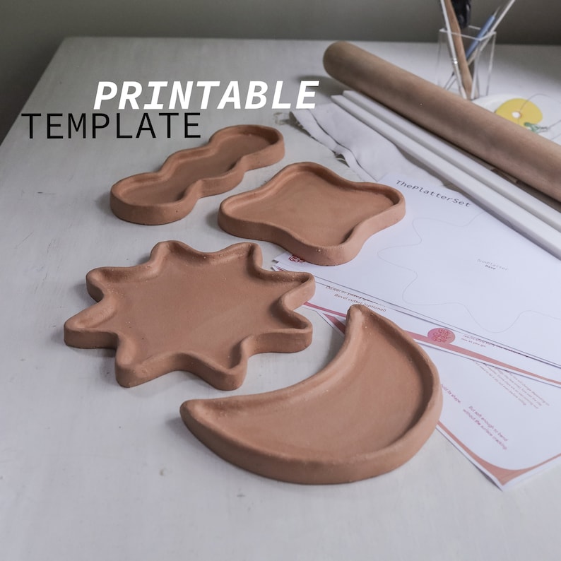 May include: Four terracotta clay trays in different shapes: a crescent moon, a star, a wavy shape, and a teardrop. The trays are on a white surface with a printed template sheet for making the trays.