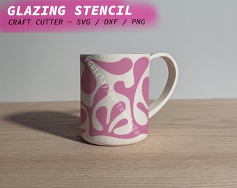 May include: A white ceramic mug with a pink abstract design. The mug has a handle and is sitting on a wooden surface. The text "@cutclaylovetemplates" is visible on the side of the mug.