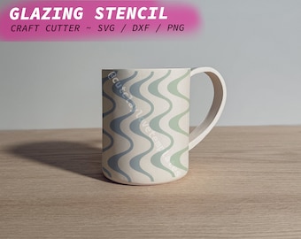 Könnte beinhalten: Eine weiße Keramiktasse mit einem wellenförmigen blauen und grünen Muster. Die Tasse hat einen Henkel und steht auf einer Holzoberfläche. Der Text "GLAZING STENCIL" befindet sich oben im Bild. Der Text "CRAFT CUTTER ~ SVG / DXF / PNG" befindet sich unter der ersten Textzeile.