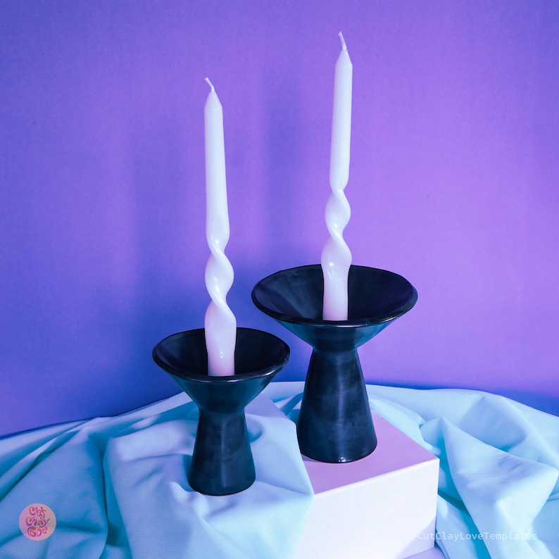May include: Two black ceramic candle holders with white twisted candles. The candle holders are on a light blue surface.